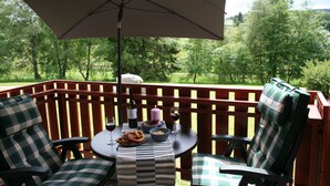 Una terraza de madera con una mesa, sillas, una botella de vino, pretzels y una vela.