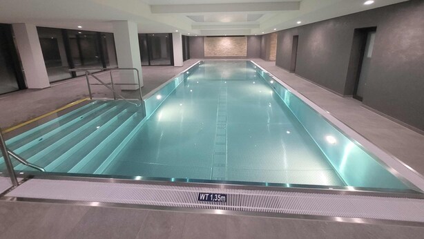 Una piscina interior con agua cristalina, un trampolín y suelo de baldosas.