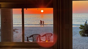 A room with a large window overlooking a beach at sunset, featuring two chairs and a bed. - Totally Remodeled Beachfront Studio-Step out your door onto the sand. Really! D (Bradenton Beach)