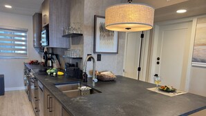 A modern kitchen with a large island, stainless steel appliances, and a hanging light fixture. - Totally Remodeled Beachfront Studio-Step out your door onto the sand. Really! D (Bradenton Beach)