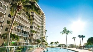A high-rise hotel with a swimming pool, palm trees, and a clear sky.