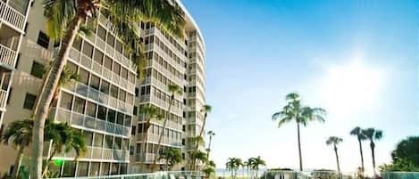 A high-rise hotel with a swimming pool, palm trees, and a clear sky.