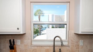 A kitchen with a window overlooking a building and palm trees.