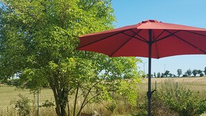 Ein draußen stehendes Holzpicknicktisch mit Bänken, einem roten Sonnenschirm und einem grünen Gießkännchen.
