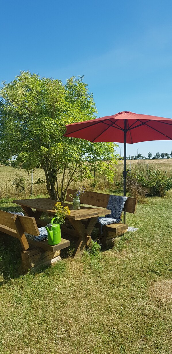 An outdoor picnic setup with a wooden table, benches, a red umbrella, and a tree in the background. - Vacation home with a large garden and a swimming lake in the village (Carmzow-Wallmow)