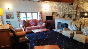 A cozy living room with a stone fireplace, a pink sofa, a television, and a patterned carpet. - In Somerset (Bristol)