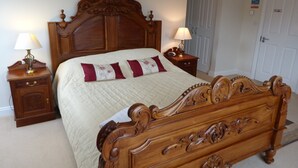 A wooden four-poster bed with a quilted bedspread and two decorative pillows. There are two bedside tables with lamps. - In Somerset (Bristol)
