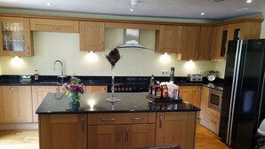 A modern kitchen with wooden cabinets, a central island, and a dining area with a table and chairs. - In Somerset (Bristol)