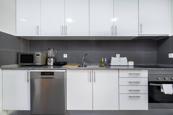 A modern kitchen with white cabinets, a built-in microwave, a coffee maker, a toaster, and a dishwasher.