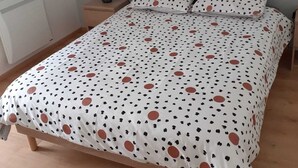 Une chambre à coucher avec un lit recouvert d’une couvre-lit à pois, une table de chevet avec une lampe et un radiateur fixé au mur.