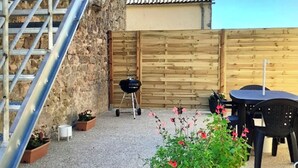 Un bâtiment en pierre avec un escalier en métal, une clôture en bois, un barbecue et des sièges d’extérieur.