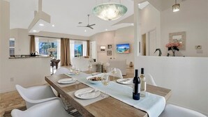 A modern dining area with a long wooden table set for a meal, white chairs, and a ceiling fan.