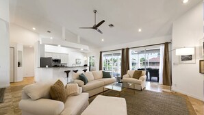 A modern living room with a sofa set, a coffee table, and a view of the kitchen and outside.