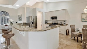 A modern kitchen with a central island, stainless steel appliances, and a dining area with wicker chairs.