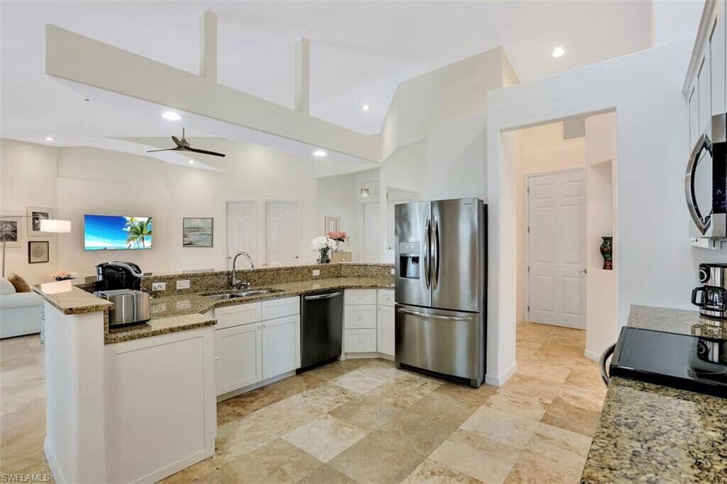 A modern kitchen with white cabinetry, a stainless steel refrigerator, granite countertops, and a ceiling fan.