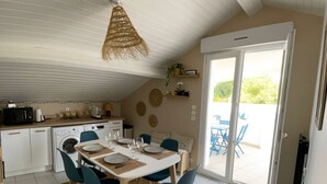 Cocina compacta con lavadora, una mesa de comedor con sillas azules y una lámpara colgante.