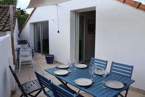 Un espace de restauration en plein air avec des tables et des chaises en métal bleu, des assiettes blanches et des verres à vin, le tout disposé pour deux personnes.