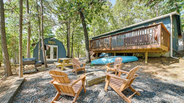Eine Hütte mit Terrasse, umgeben von Bäumen, mit Holzsesseln und einem Feuerkorb.