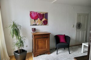 Une pièce comprenant un pot de fleurs, un meuble en bois, une chaise noire avec un coussin rouge et un tableau abstrait accroché au mur.
