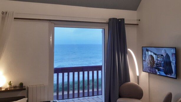A room with a view of the sea, a bed, a desk, a chair, and a TV on the wall. - Beachfront apartment on Juno Beach (Bernières-sur-Mer)
