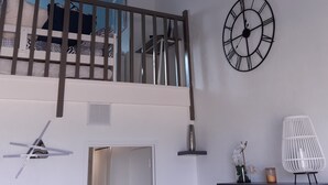 A room with a white wall, a black clock, a white chair, and a door. - Beachfront apartment on Juno Beach (Bernières-sur-Mer)