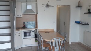 A compact kitchen with a dining area, a built-in oven, and a microwave. - Beachfront apartment on Juno Beach (Bernières-sur-Mer)