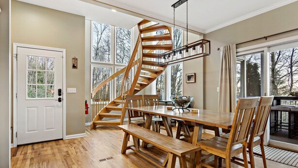 Ein geräumiger Essbereich mit einer Holzbänkl und einem Tisch, einer Wendeltreppe und großen Fenstern mit Blick auf Bäume.
