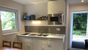 A modern kitchen with a built-in microwave, stainless steel sink, and white cabinetry. There is a window providing natural light and a view of greenery outside.