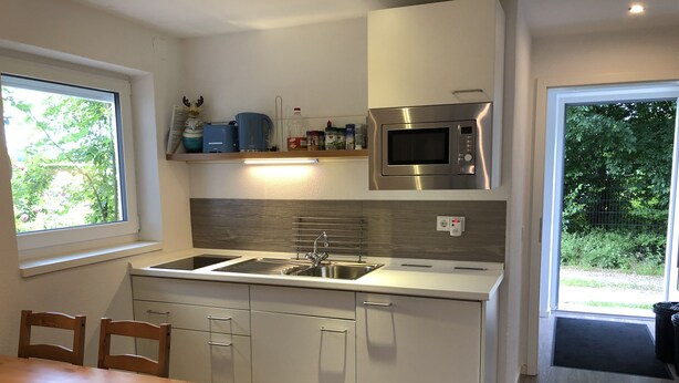 Een moderne keuken met een ingebouwde magnetron, een roestvrijstalen spoelbak en witte kasten. Er is een raam dat natuurlijk licht en uitzicht op groen biedt.