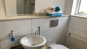 Een badkamer met een witte wastafel, toilet, spiegel en een handdoekrek met handdoeken.