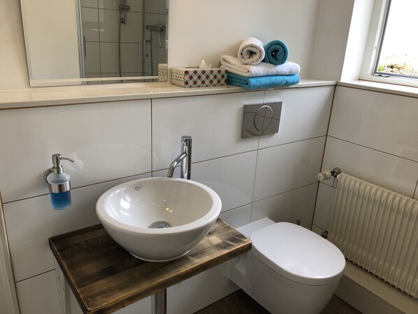 Un baño con un lavamanos blanco, un inodoro, un espejo y un perchero con toallas.