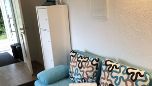 Een kamer met een lichtblauwe bank, gestreepte kussens, een witte kast en een zwarte prullenbak.