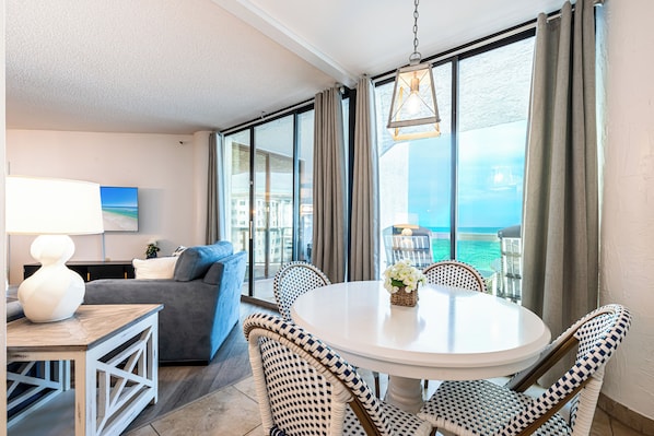 A hotel room with a balcony, a round dining table, wicker chairs, a sofa, and a view of the ocean.
