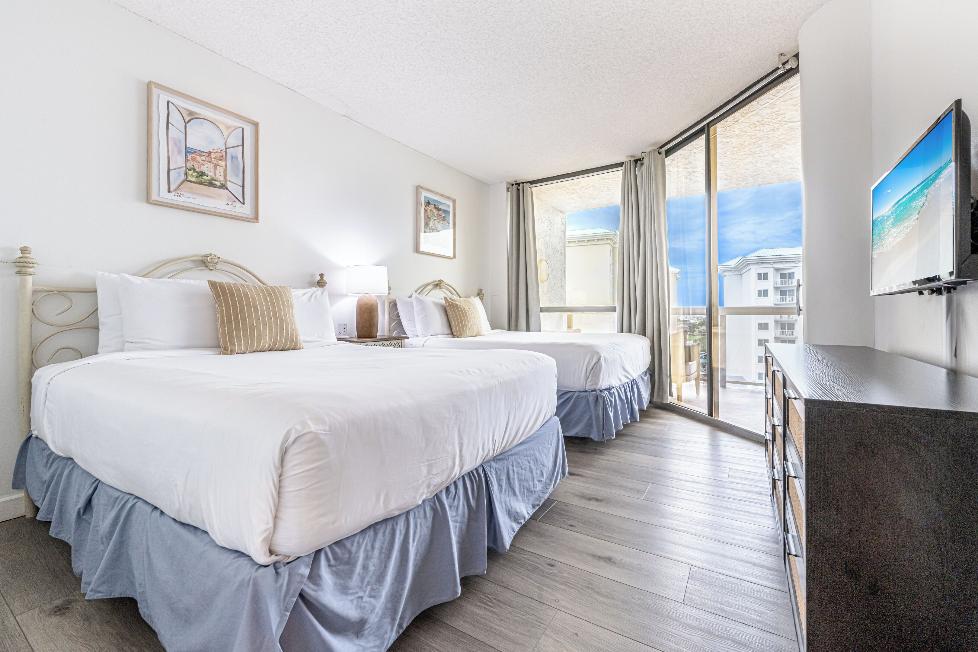 A hotel room with two beds, a large window, and a flat-screen TV.
