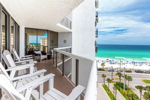 A balcony with white Adirondack chairs, a small table, and a view of the ocean and beach.