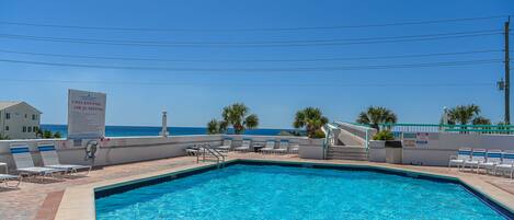 A clear blue pool with lounge chairs and a sign prohibiting diving or jumping.