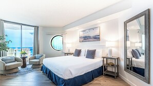 Quarto de hotel moderno com uma cama grande, duas poltronas, um espelho redondo e vista para a cidade.