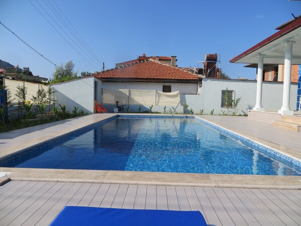 Relax by the pool surrounded by lush greenery and a tiled deck.