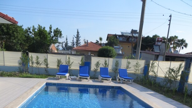Una piscina rectangular con agua azul cristalina, rodeada por una solana con baldosas. Hay sillas reclinables azules alineadas a lo largo del borde de la piscina.