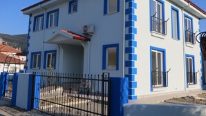 Un edificio de dos pisos con paredes exteriores azules y blancas, múltiples ventanas y una cerca de metal negro.