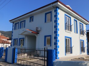 Two-story building with a flat roof and blue-framed windows, surrounded by a black iron fence.