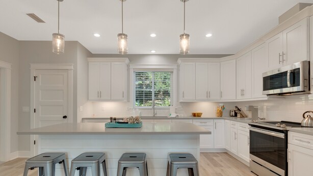 A modern kitchen with white cabinets, a large island with bar stools, stainless steel appliances, and pendant lighting. - New Build • Walk to the beach• Bikes • Beach Toys! (St. Augustine)