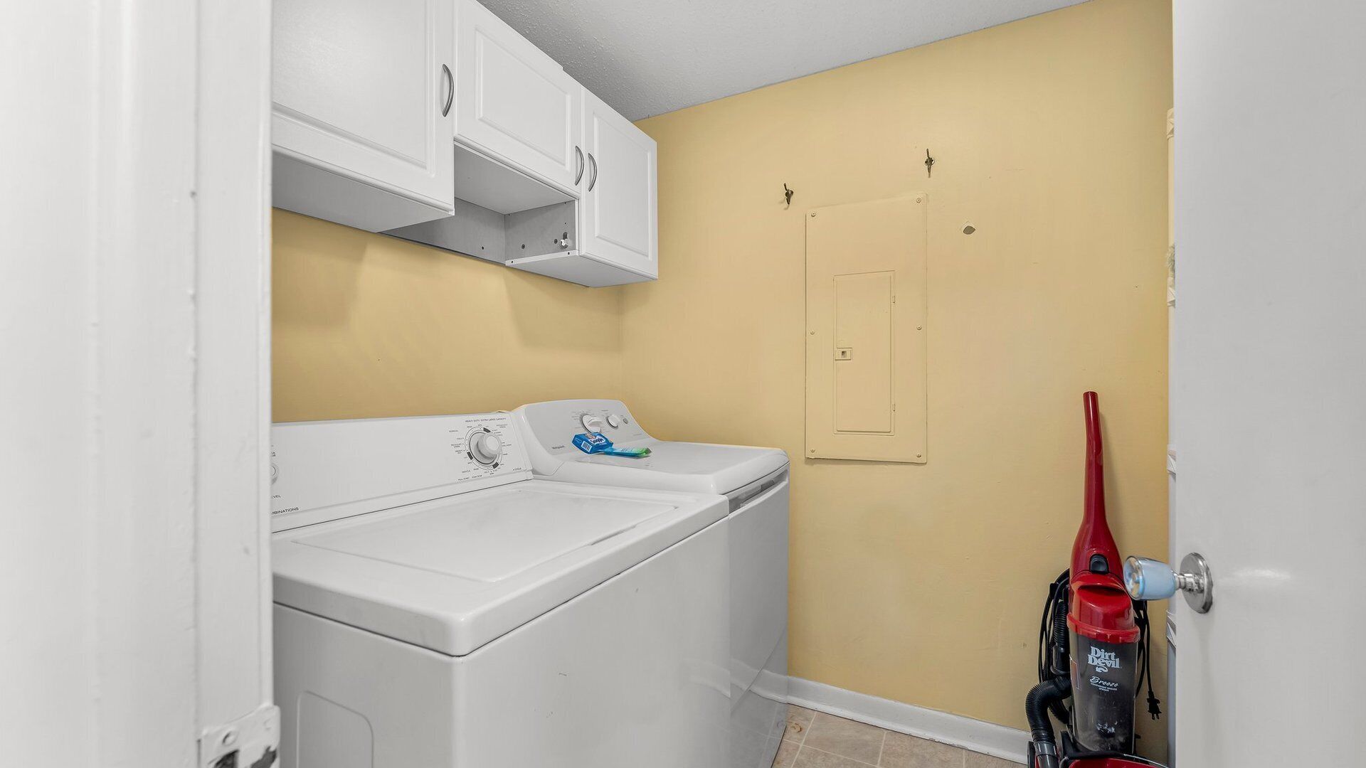 Une buanderie équipée d’un lave-linge et d’un sèche-linge à chargement frontal, d’un aspirateur rouge et d’un mur jaune.