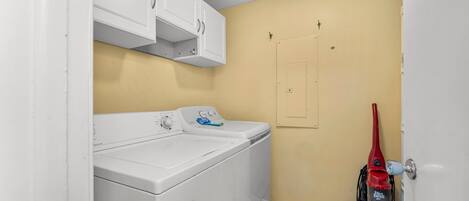Une buanderie équipée d’un lave-linge et d’un sèche-linge à chargement frontal, d’un aspirateur rouge et d’un mur jaune.