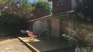Une terrasse en bois avec deux chaises et une table, entourée d’arbres.