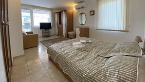 Habitación de hotel con cama, televisor, armario, espejo y ventana con persianas.