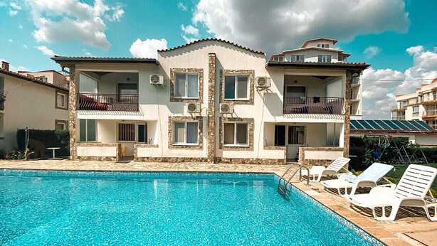 Una piscina con sillones de descanso y un edificio con balcones al fondo.