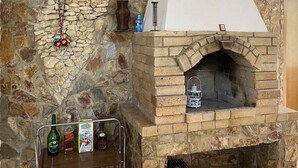 Una chimenea de piedra con una chimada blanca, un estante de metal con botellas y un adorno colgante en la pared.