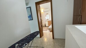 Un pasillo estrecho con un banco, una puerta que da a un dormitorio y una encimera blanca a la derecha.