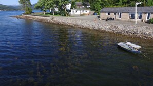 Ein Anwesen am Seeufer mit Steinmauer, einer Reihe von Häusern und einem Boot, das in der Nähe des Ufers liegt.